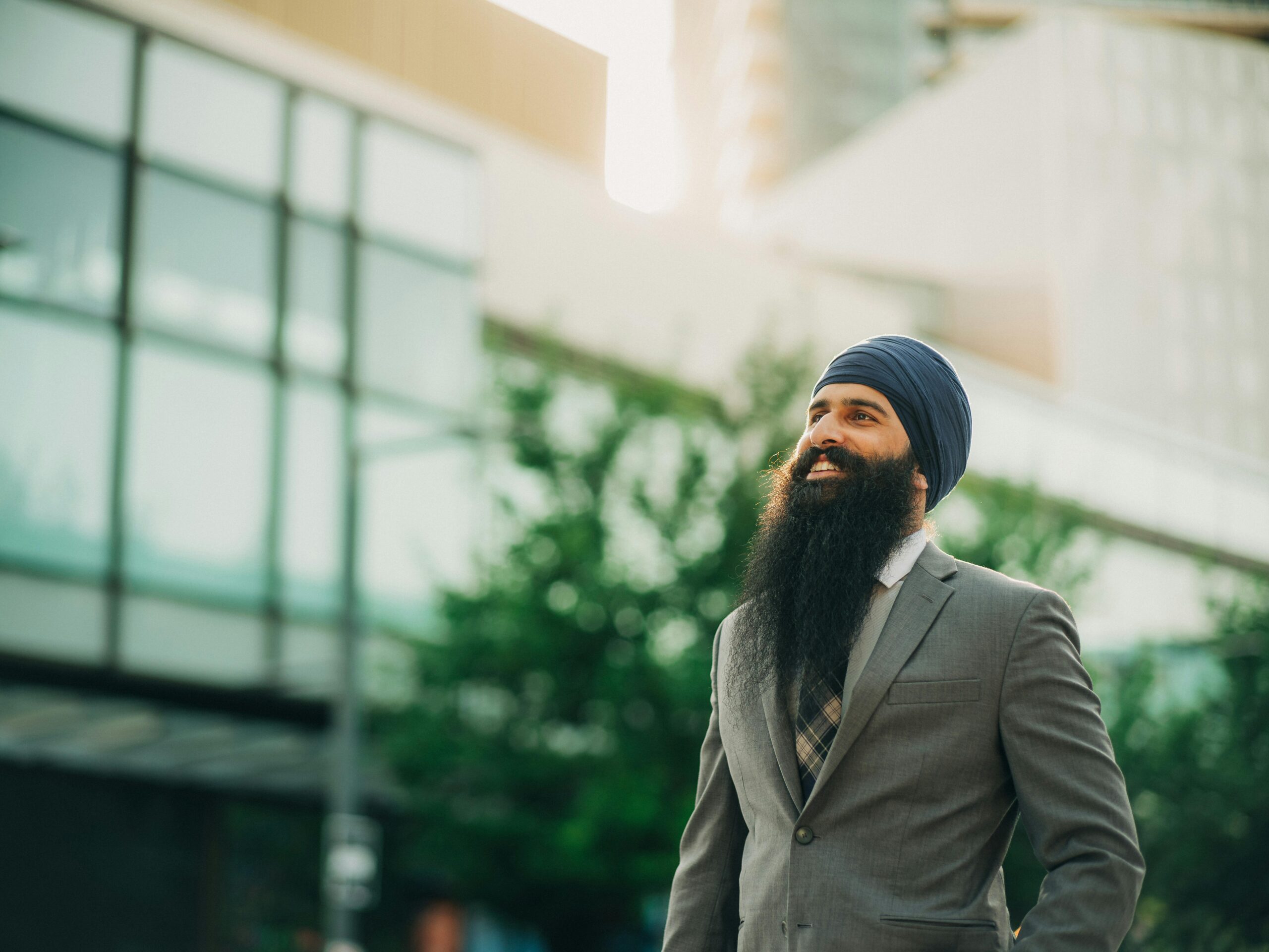 Home Adult Sikh man in formal suit smiling under sunlight, depicting confidence in an urban setting.