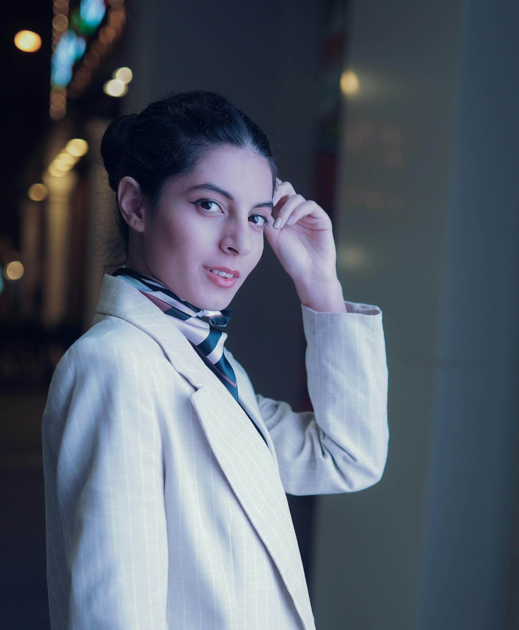 Home Portrait of a stylish woman in a light suit and scarf, posing outdoors at night in Dubai.